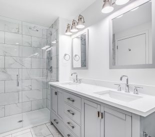 An elegant, remodeled bathroom with a grey vanity and bronze har An elegant, remodeled bathroom with a grey vanity and bronze har