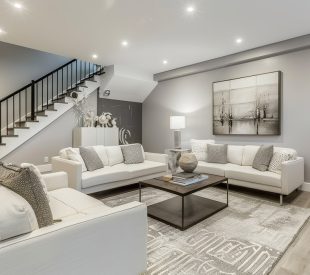 An interior shot of a recently renovated basement with contempor An interior shot of a recently renovated basement with contemporary design elements, including a large white sectional sofa and gray-toned wood-look flooring