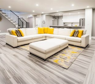 An interior shot of a recently renovated basement with contempor An interior shot of a recently renovated basement with contemporary design elements, including a large white sectional sofa and gray-toned wood-look flooring
